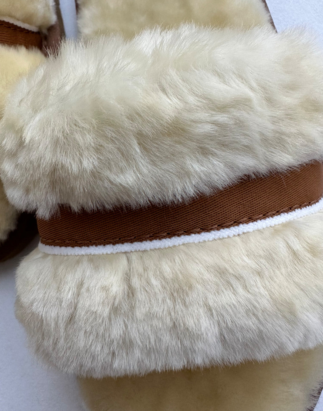 Nahaufnahme des flauschigen, cremefarbenen Stoffes mit kontrastierenden braun-weißen Streifen, wahrscheinlich Teil der gemütlichen Schlappen in Beige/Creme von LIRA Deko. Die Textur ist kuschlig und plüschig und vermittelt Wärme und Behaglichkeit.